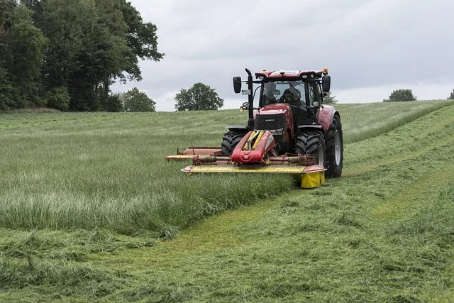 Traktor koszący łąkę w lipcu podczas drugich sianokosów